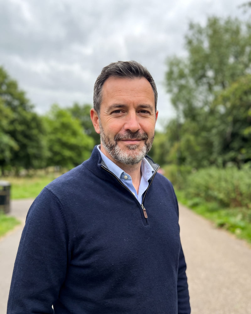 A casual phone photo of a smiling man with a salt-and-pepper beard in a navy sweater, in a park